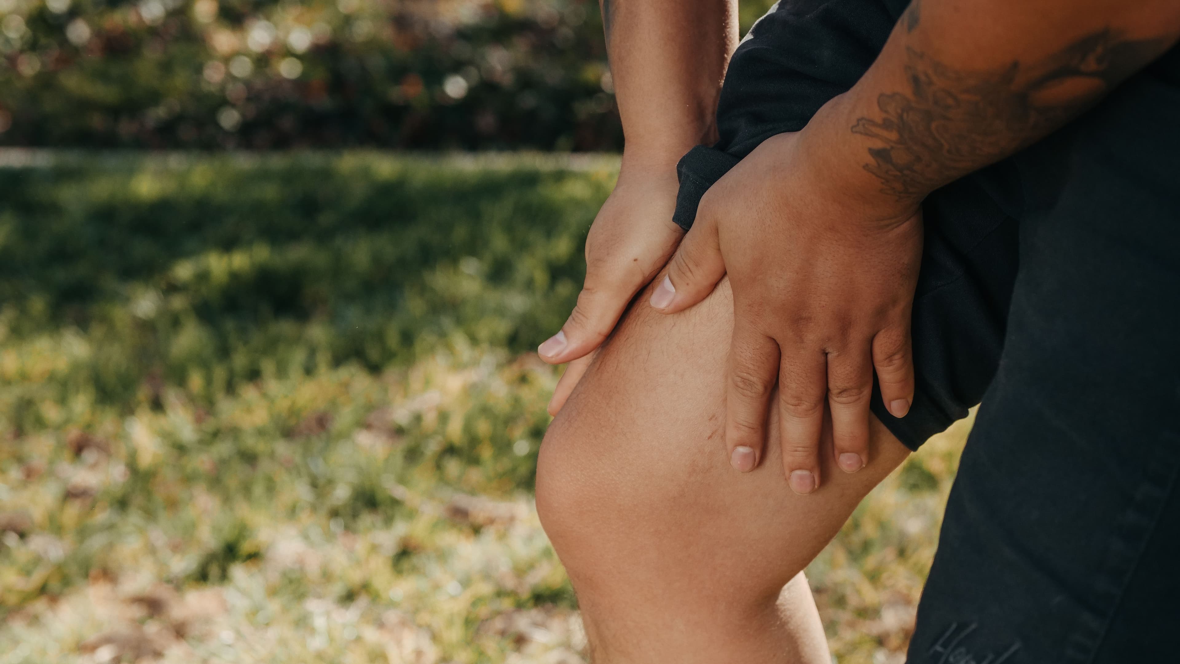 An adult holding a painful knee outdoors